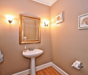 Bathroom with brown walls wood floors white pedestal sink with mirror above it white baseboards