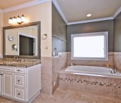 Bathroom with brown tile for the floors around bathtub and halfway up wall window above bathtub green and yellow walls white cabinets with gray countertop