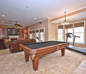 Room with brown walls recessed lighting ceiling fan windows with brown shades brown carpet and pool table treadmill and leather couch