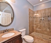 Bathroom with brown tile floor and shower with glass door brown cabinet with brown granite countertop white toilet light blue walls