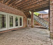 Back patio on a brick home with double doors leading out to it large windows cement floors and brick columns
