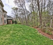 Back of a brown brick two story home with green grass and trees on the border of the yard