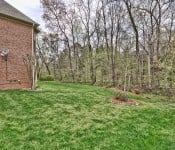 Backyard of a brown brick home with a satellite dish on the side green grass and trees