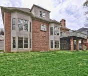 Back of brown two story brick home with covered patio and second story gray painted deck
