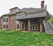 Back of brown two story brick home with covered patio and second story gray painted deck