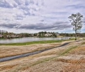 Golf course with grass and trees and a cloudy sky with a lake pathway and home in the background
