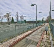 Green tennis courts with green lamp posts and green fence with gravel lined cement pathway around it with green benches