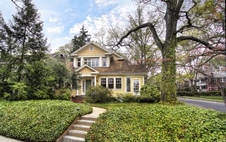 Two story yellow siding house with white trim dark brown shingle roof green front door steps to front door
