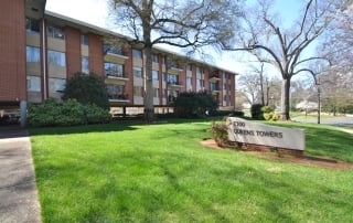 Brick condo building with patios and large green lawn and Queens Towers sign in front