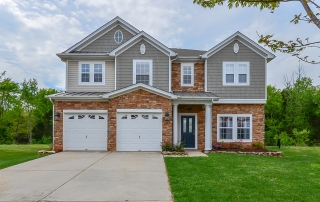 Two story home with brown stone on first floor gray shingles and yellow siding on second floor two garages with blue front door