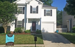 Two story white siding home with black shutters black mailbox driveway with one car garage white fenced in backyard blue and brown Savvy sign in front