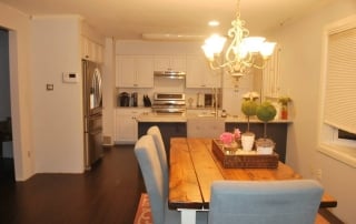 Kitchen with white cabinets new stainless steel appliances navy blue island gray countertops open to dining room with wood table and blue chairs