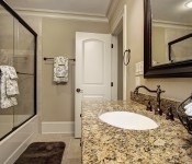 Bathroom with light brown cabinets brown granite countertop dark wood framed mirror bathtub with glass wall