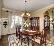 Dining room with dark wood floors chandelier over table cherry wood furniture window with white curtains in front white chair molding high up walls