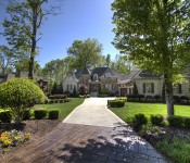 Front of large three story brick and stone home with three car garage and manicured front lawn with long driveway