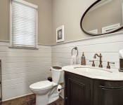 Bathroom with light brown walls white paneling halfway up wall dark wood floors dark wood cabinets with granite countertop window above toilet