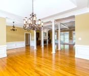 Empty dining room with wood floors yellow walls white chair molding white columns large chandelier in middle of the room open to living room