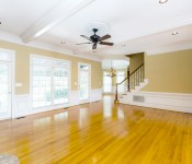 Empty living room with wood floors yellow walls white chair molding large windows and doors to backyard brown ceiling fan