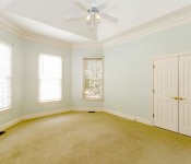 Empty room with light sea-foam green walls yellow carpet white baseboards white trim windows white double doors with gold door handles tray ceiling with white ceiling dan
