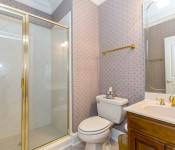 Bathroom with white toilet gold fixtures dark wood cabinet white countertops white tile shower with gold frame glass shower door