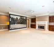 Large empty room with brown walls brown wallpapers with dark wood cabinets built in fireplace with white mantle black and white golf mural