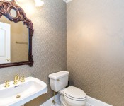Powder room with gray wallpaper white pedestal sink white toilet gold hardware wood frame mirror