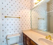 Bathroom with shell wallpaper dark wood cabinets white countertops gold hardware white toilet