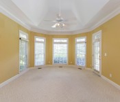 Master bedroom with white carpet flooring yellow walls white tray ceiling white ceiling fan pay windows