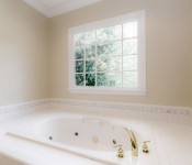 Bathroom with yellow walls soaking bathtub with tile around it and window over tub