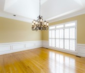 Empty dining room with wood floors yellow walls white chair molding three windows with white blinds chandelier in the middle of the room