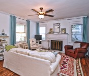 Living room with white walls white molding wood floors dark brown ceiling fan white sofa brown leather armchair orange pink and white rug fireplace with white mantle