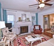 Living room with white walls white molding wood floors dark brown ceiling fan white sofa brown leather armchair orange pink and white rug fireplace with white mantle