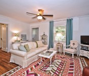 Living room with white walls white molding wood floors dark brown ceiling fan white sofa brown leather armchair orange pink and white rug