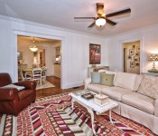 Living room with white walls white molding wood floors dark brown ceiling fan white sofa brown leather armchair orange pink and white rug