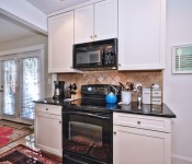Kitchen with white cabinets black countertops black oven black microwave tile flooring light brown walls