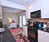 Kitchen with white cabinets black countertops black fridge tile flooring light brown walls open to room with blue sofa and art gallery wall