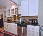 Kitchen with white cabinets black countertops black fridge tile flooring light brown walls open to room with blue sofa and art gallery wall