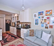 Kitchen with white cabinets black countertops black fridge tile flooring light brown walls open to room with blue sofa and art gallery wall