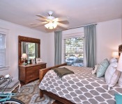 Bedroom with white walls white ceiling fan two windows wood floors wood bed and dresser