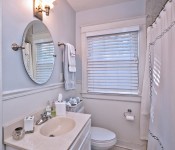 Bathroom with white walls white cabinets white countertop oval mirror window above toilet