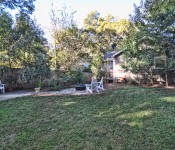 Backyard with green grass and trees hammock and fire pit shed and white bench