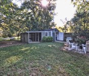 Backyard with green grass and trees hammock and fire pit open shed with eating area