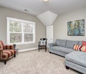 Living room with gray walls white door white baseboards white trim window carpet flooring gray sofa red striped armchair
