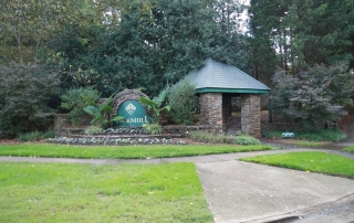 Large stone sign that says Thornhill in green and gold stone sitting area with green roof trees and green grass around it and cement sidewalk