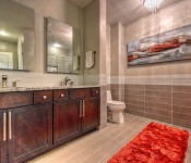Bathroom with gray tile floors and half wall with gray tile half with gray paint white door dark brown wood cabinets gray granite countertops area for toilet orange rug