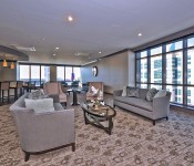 Large room with gray sofas brown chairs sitting area and bar area with brown carpet brown paint large floor to ceiling windows