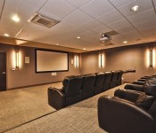 Theater room brown walls carpet flooring brown leather reclining seats overhead projector large movie screen