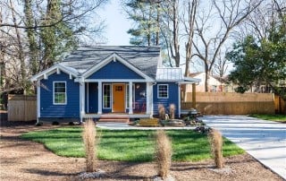 Blue siding home with blue shingle details and white trim driveway on the side fenced in backyard orange front door