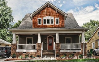 Two story home with gray siding white trim windows white columns and railing on front porch brown stone around foundation brown shingles on second floor