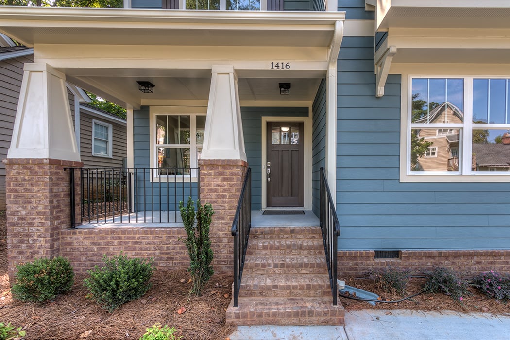 Home with blue siding brown brick around porch and foundation brown front door white trim black iron railing
